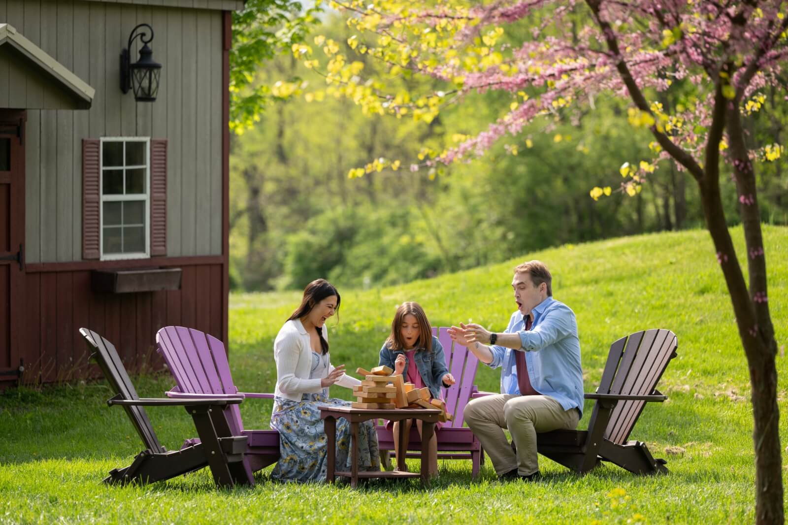 A family reacts with surprise as a wooden block tower tumbles on an outdoor table