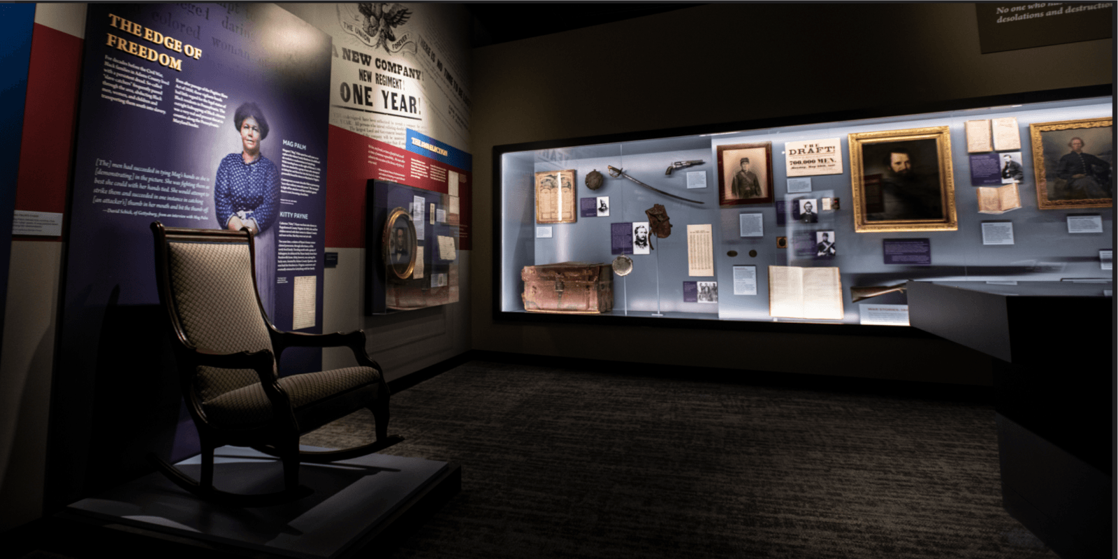 An indoor museum exhibit displaying historical artifacts, information walls, and a rocking chair