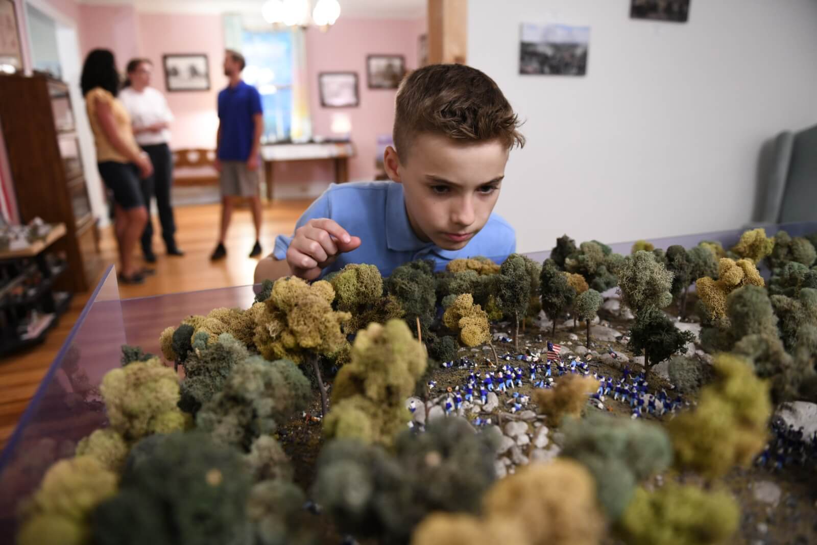 A young boy looks closely at a miniature Gettysburg battlefield diorama with tiny soldiers and trees