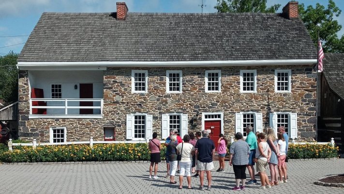 A tour group stands outside a historic two-story fieldstone house with white shutters and a red door