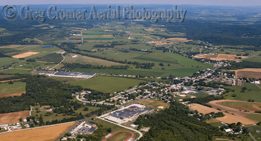 An aerial view shows a town surrounded by green and gold farm fields