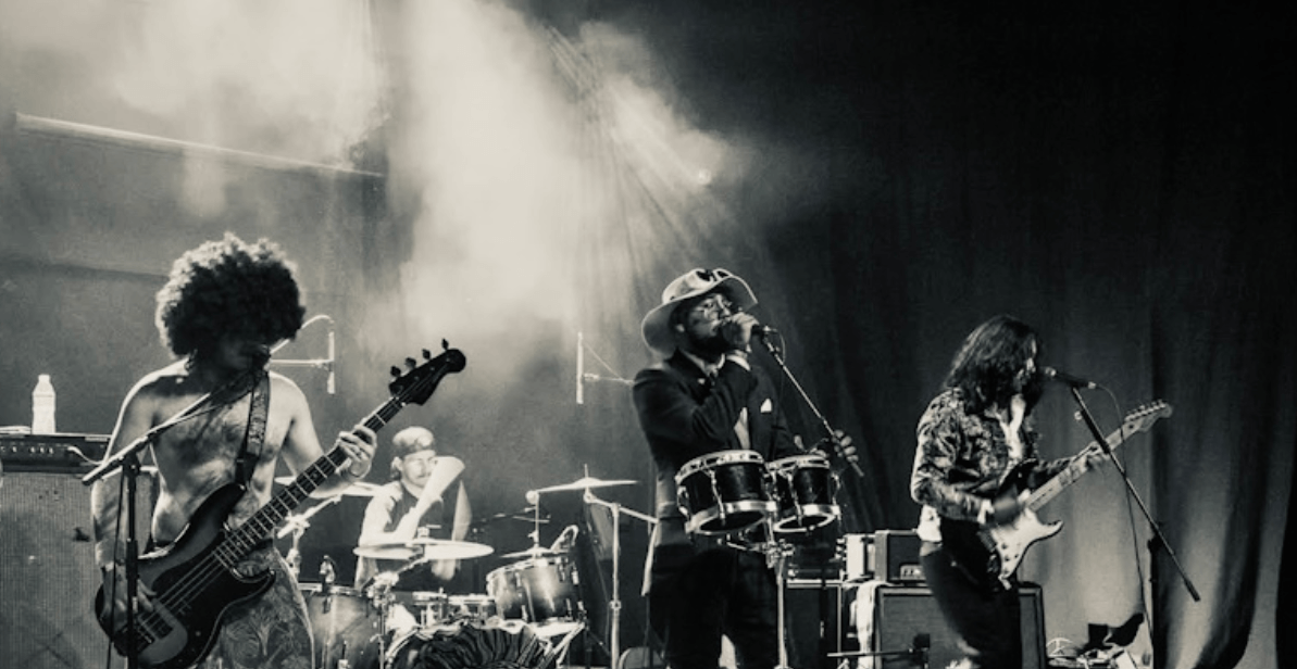 A band performs on a smoky stage in a black-and-white photo