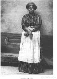 Historic portrait of a woman in a patterned dress and apron with hands clasped